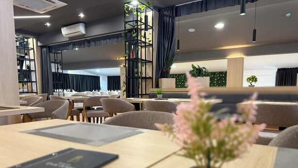 Un'area ristorazione moderna con tavoli, sedie, una pianta in vaso e un menu sul tavolo.
