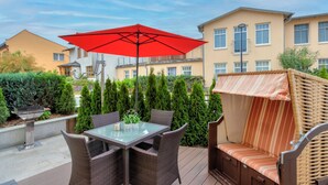 Eine Terrasse im Freien mit einem Glastisch, Korbstühlen, einem roten Sonnenschirm und einer Korbschaukel.