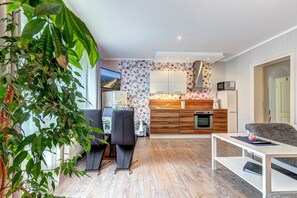 A modern living room with a dining area, a kitchen with wooden cabinets, and a large window with a view. - 2-bedroom vacation apartment, Wi-Fi, near the beach, garage, terrace, beach chair (Heringsdorf)
