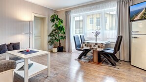 Ein modernes Wohnzimmer mit Essbereich, einem großen Fenster mit Vorhängen, einem Flachbildfernseher und einem Kühlschrank.
