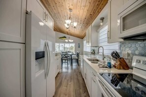 A modern kitchen with white cabinetry, a wooden ceiling, and a view to the outside.
