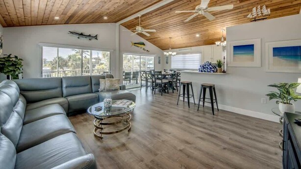 Un espacio habitable amplio con techo de madera, sofá de cuero, mesa de comedor y taburetes de bar.