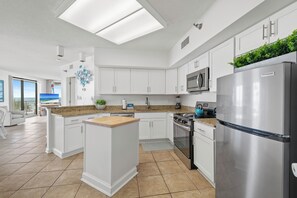 Una cocina moderna con armarios blancos, un refrigerador de acero inoxidable, un microondas integrado y una isla grande con encimera de madera.