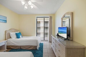 A bedroom with a bed, a dresser, a television, a mirror, and a balcony door.
