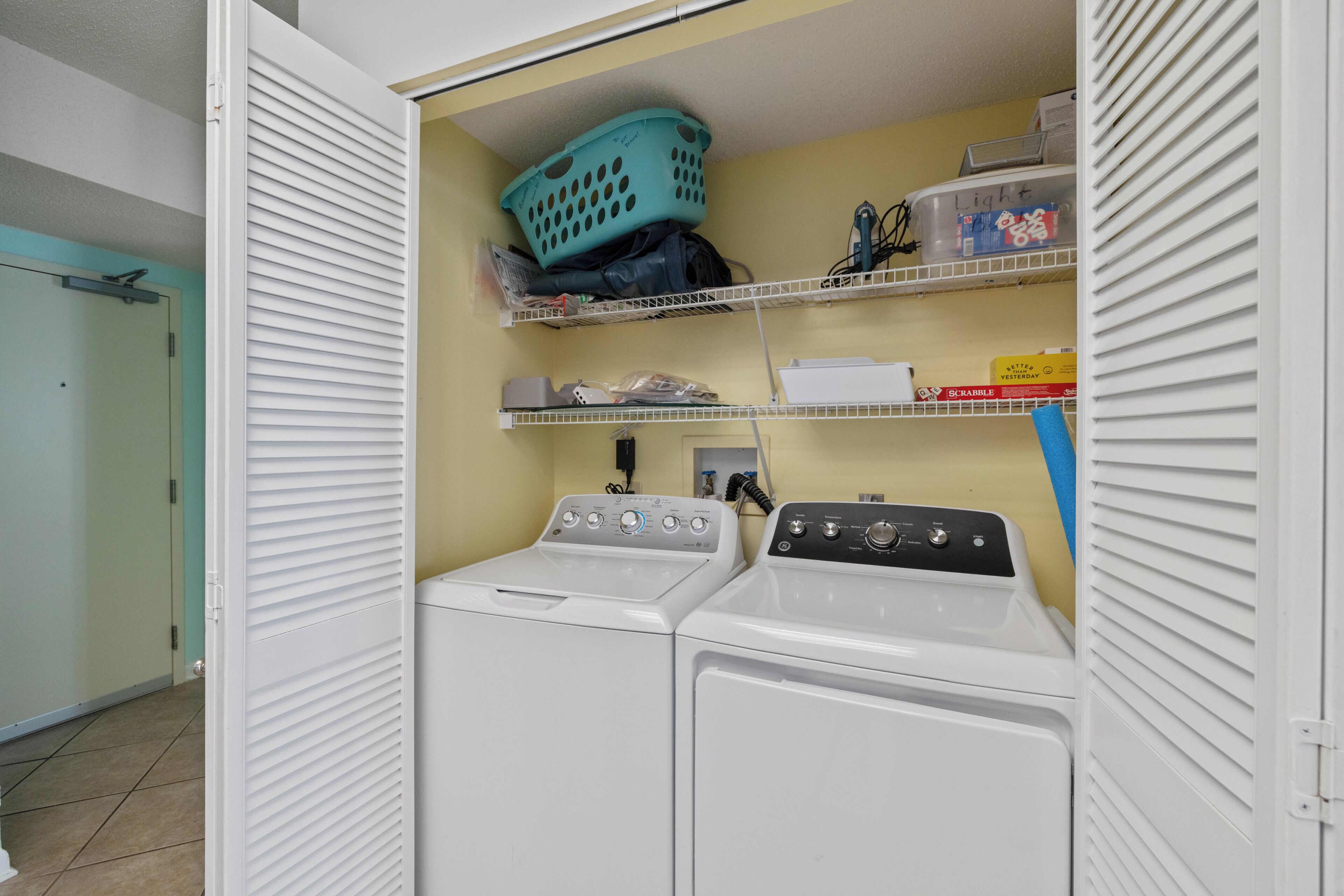 A laundry room with two washing machines, shelves with laundry supplies, and a basket on the top shelf.
