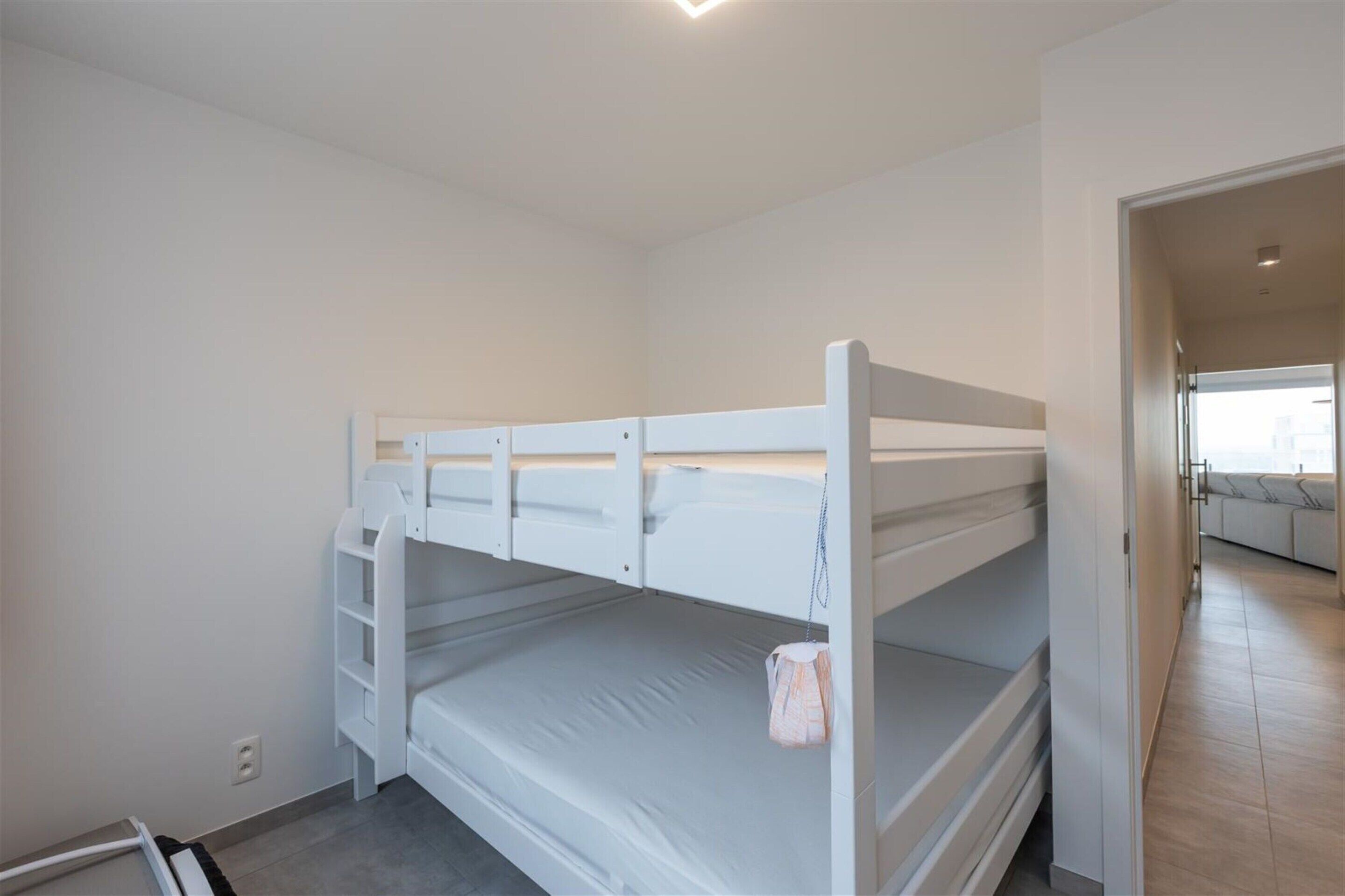 A bunk bed room with a white color scheme, a small closet, and a door leading to another room.