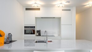 A modern kitchen with white cabinetry, a built-in oven, a coffee maker, and a sink.