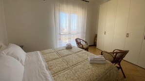 A bedroom with a bed, a chair, a wardrobe, and a window with curtains.