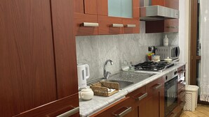 A kitchen with wooden cabinets, a stainless steel range hood, a microwave, and a tiled floor.