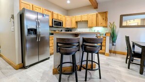 A modern kitchen with wooden cabinets, a stainless steel refrigerator, a microwave, and two bar stools. - Dog friendly, hot tub, free shuttle (Keystone)