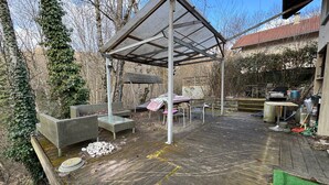 Una terraza de madera con mobiliario exterior, un espacio de estar cubierto y un jardín.