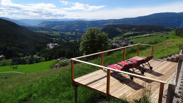 A wooden deck with a red lounge chair and a table, overlooking a valley with mountains in the background. - Apartment 'Schmetterling' with Mountain View, Shared Terrace and Wi-Fi (Seis)