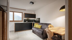 A compact kitchen with a dark grey sofa, wooden dining table, and a view of mountains through a window. - Apartment 'Schmetterling' with Mountain View, Shared Terrace and Wi-Fi (Seis)