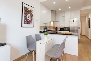 Una cocina moderna con armarios blancos, una isla central, sillas grises y una mesa de comedor.