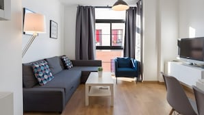 A modern living room with a sofa, a coffee table, a TV, and a view of a red building through large windows. - Apartment 'Quiet, Bright and Central' with Shared Terrace, Wi-Fi and Air Conditioning (Málaga)