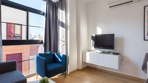 A modern living room with a TV on a white wall, a blue sofa, and a balcony with a view of buildings. - Apartment 'Quiet, Bright and Central' with Shared Terrace, Wi-Fi and Air Conditioning (Málaga)