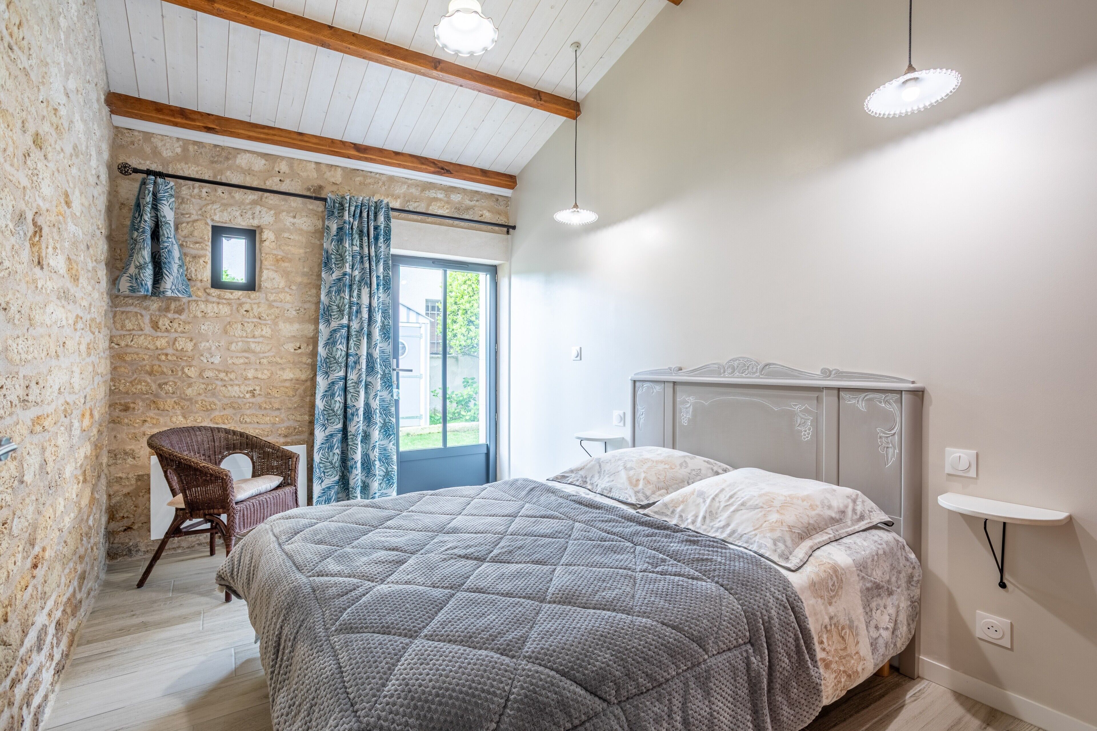 A bedroom with a bed, a chair, a small window, and a stone wall.