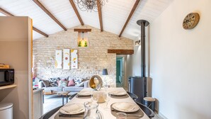 Comedor con pared de piedra, vigas de madera, una araña y un rústico hogar.
