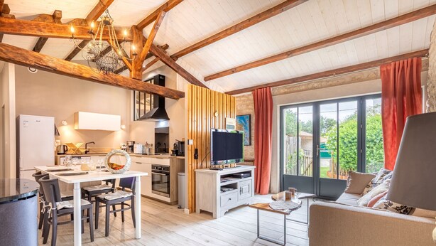 Amplia sala de estar con mesa de comedor, cocina y un ventanal con cortinas.
