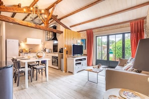A spacious living area with a dining table, kitchen, and a large window with curtains. - The Chai de la Lumineuse – Authentic Home in Saint-Pierre-d'Oléron, Tranquility & Comfort (SAINT PIERRE D'OLERON)