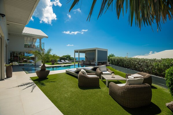 Relax in a serene outdoor space with a pool, lawn, and comfortable wicker sofas.
