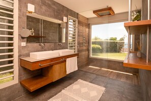 Features a wall-mounted mirror, wooden vanity, and large window with an outdoor view.