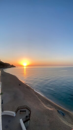 Una playa con un atardecer, un sendero curvo y una barandilla.