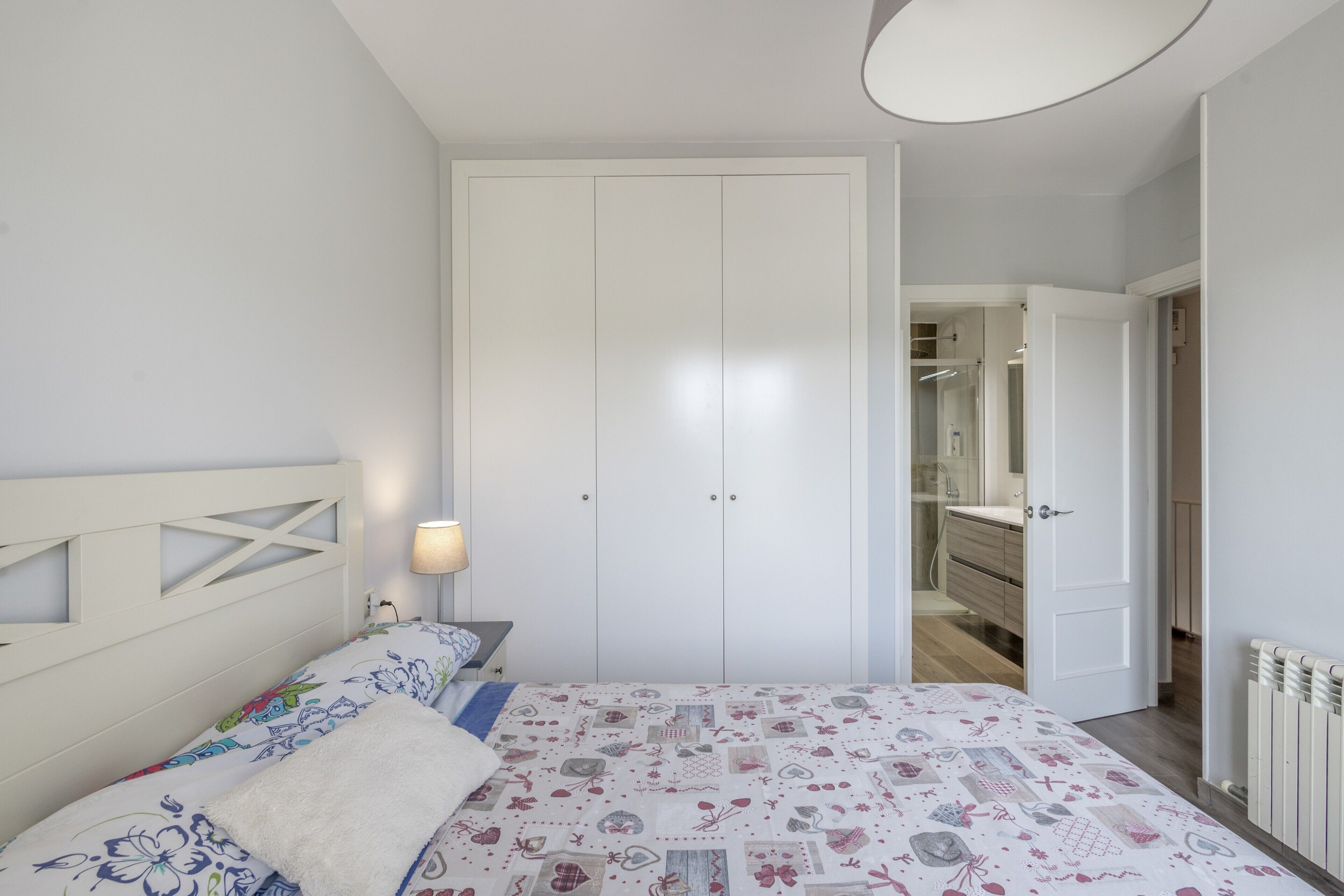 Et soveværelse med en seng, et sengebord, en lampe og et klædeskab.