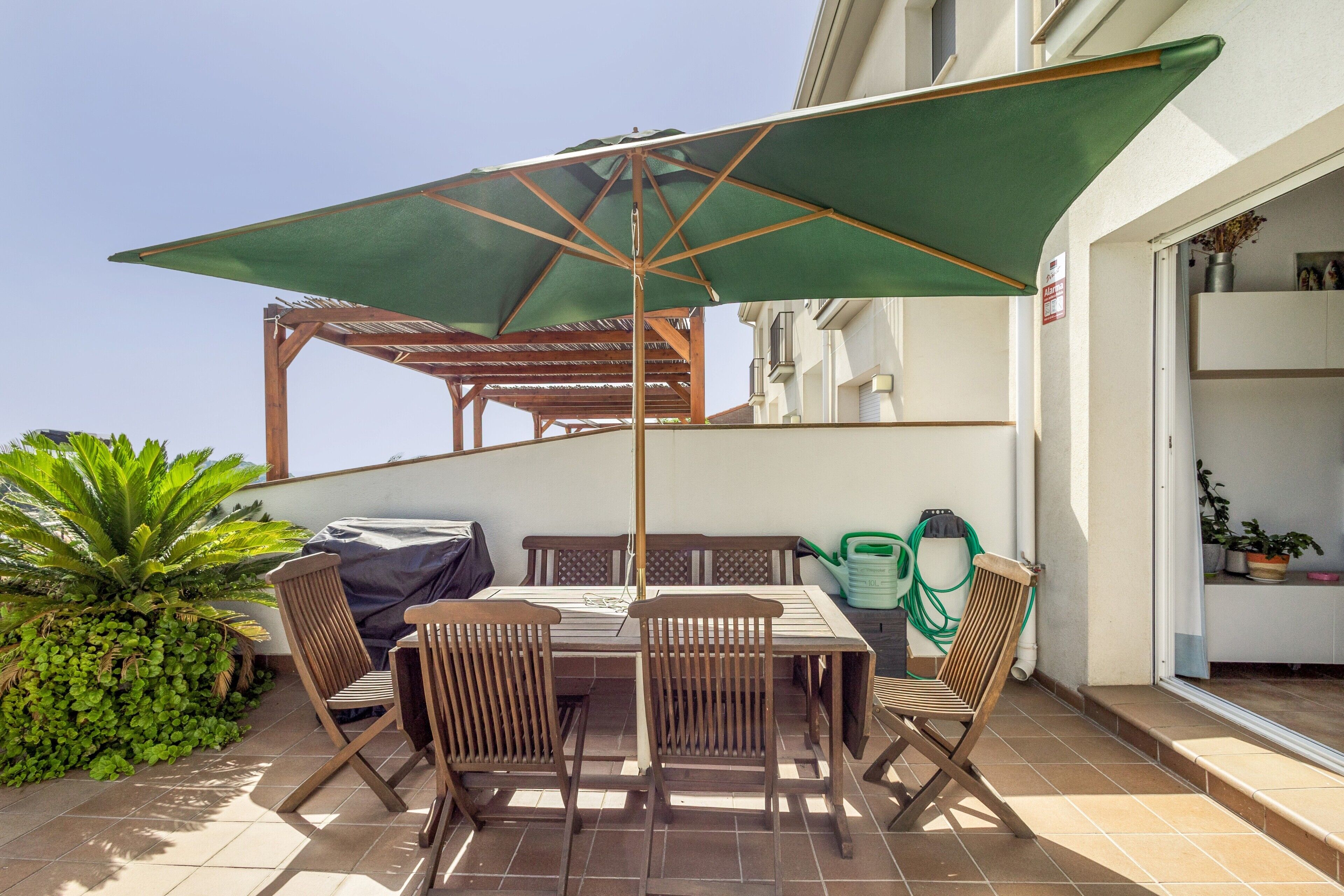 An outdoor patio with a table and chairs, a green umbrella, and a pergola structure.