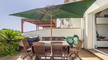An outdoor patio with a table and chairs, a green umbrella, and a pergola structure.