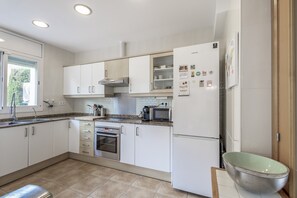 A modern kitchen with white cabinets, a stainless steel oven, a microwave, and a refrigerator.