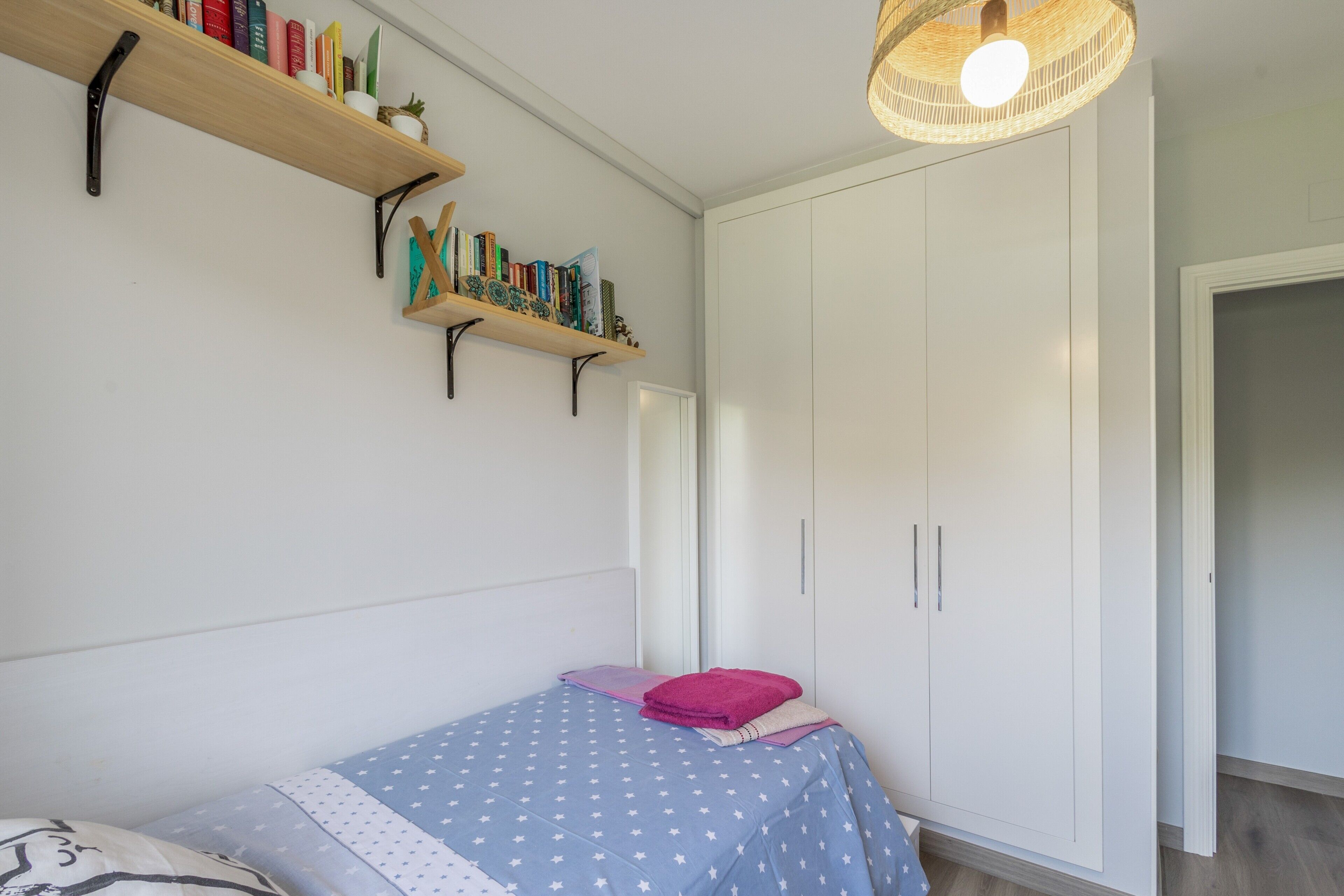 Un dormitorio con cama, armario y estantería con libros.