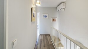 Un pasillo con piso de madera, paredes blancas y barandal blanco. Se observan tres cuadros enmarcados en la pared.