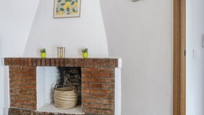 A brick fireplace with two potted plants on top, a framed picture above it, and a basket below. - Holiday Home 'Manuel' with Shared Pool, Wi-Fi and Air Conditioning (Conil)
