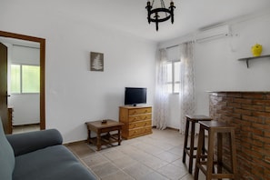 A living room with a sofa, a TV on a wooden cabinet, a small table, and a brick fireplace.