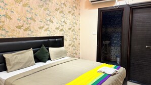 Ein Schlafzimmer mit einem Bett, Kissen, einem gestreiften Handtuch, einer dunklen Tür und einem Badezimmer mit Waschbecken und Dusche.
