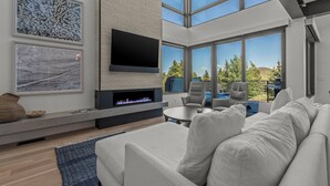 A modern living room with a fireplace, comfortable seating, and large windows offering a view of the outdoors. - Modern Home in Canyons Village by InvitedHome | Hot Tub, Game Room, Hike, Bike (Park City)