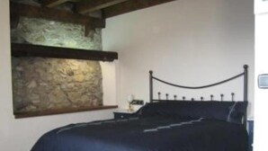 A bedroom with a stone wall, a bed with a headboard, and a nightstand.