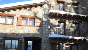 A stone building with multiple balconies, wooden shutters, and a snow-covered roof.