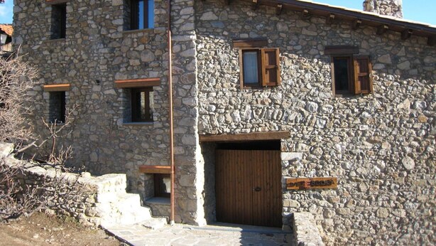 Un bâtiment en pierre avec une porte en bois, de nombreuses fenêtres et une cheminée.