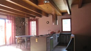 Une cuisine avec des poutres en bois, un mur en pierre, un coin repas avec des chaises et une fenêtre.