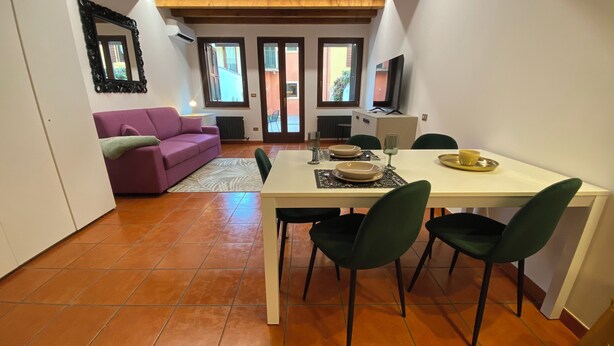 Uma sala de jantar com uma mesa posta para quatro pessoas, um sofá roxo e vista para o exterior através de uma porta.
