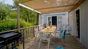 Eine überdachte Terrasse im Freien mit Tisch, Stühlen, Grill und Blick auf ein Haus im Hintergrund.