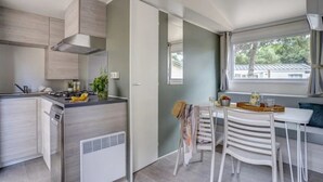 Eine kompakte Küche mit modernen Geräten, ein Essbereich mit Tisch und Stühlen sowie ein Fenster mit Blick ins Grüne.