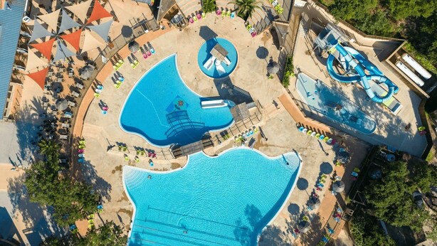 An aerial view of a resort with multiple swimming pools, sun loungers, and shaded areas.