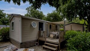 A mobile home with a deck, a small table, and a lounge chair.