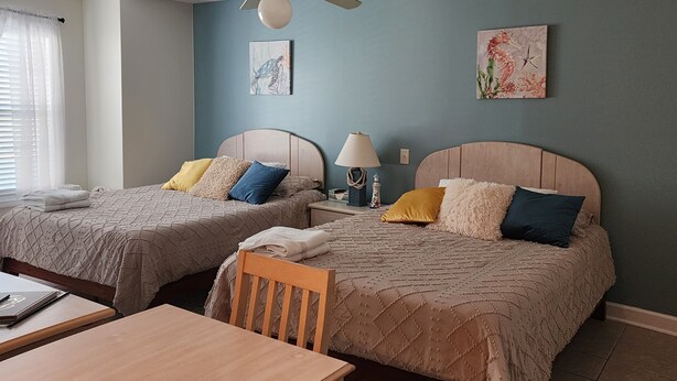 A bedroom with two beds, a ceiling fan, and artwork on the walls.