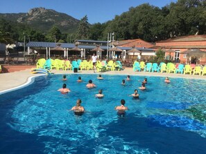 Une piscine où des personnes nagent, entourée de chaises colorées et de bâtiments aux toits rouges.