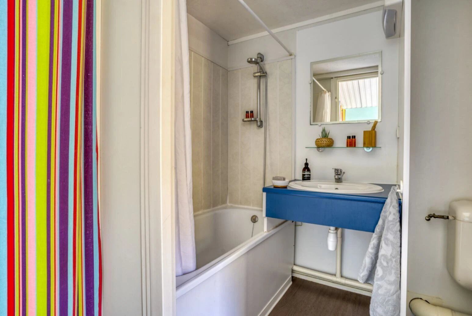 Une salle de bain avec une baignoire, un lavabo et des toilettes. Il y a une pomme de douche au-dessus de la baignoire et un miroir au-dessus du lavabo.