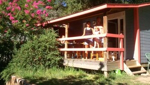 Una cabaña de madera con porche, rodeada de vegetación y flores rosadas.